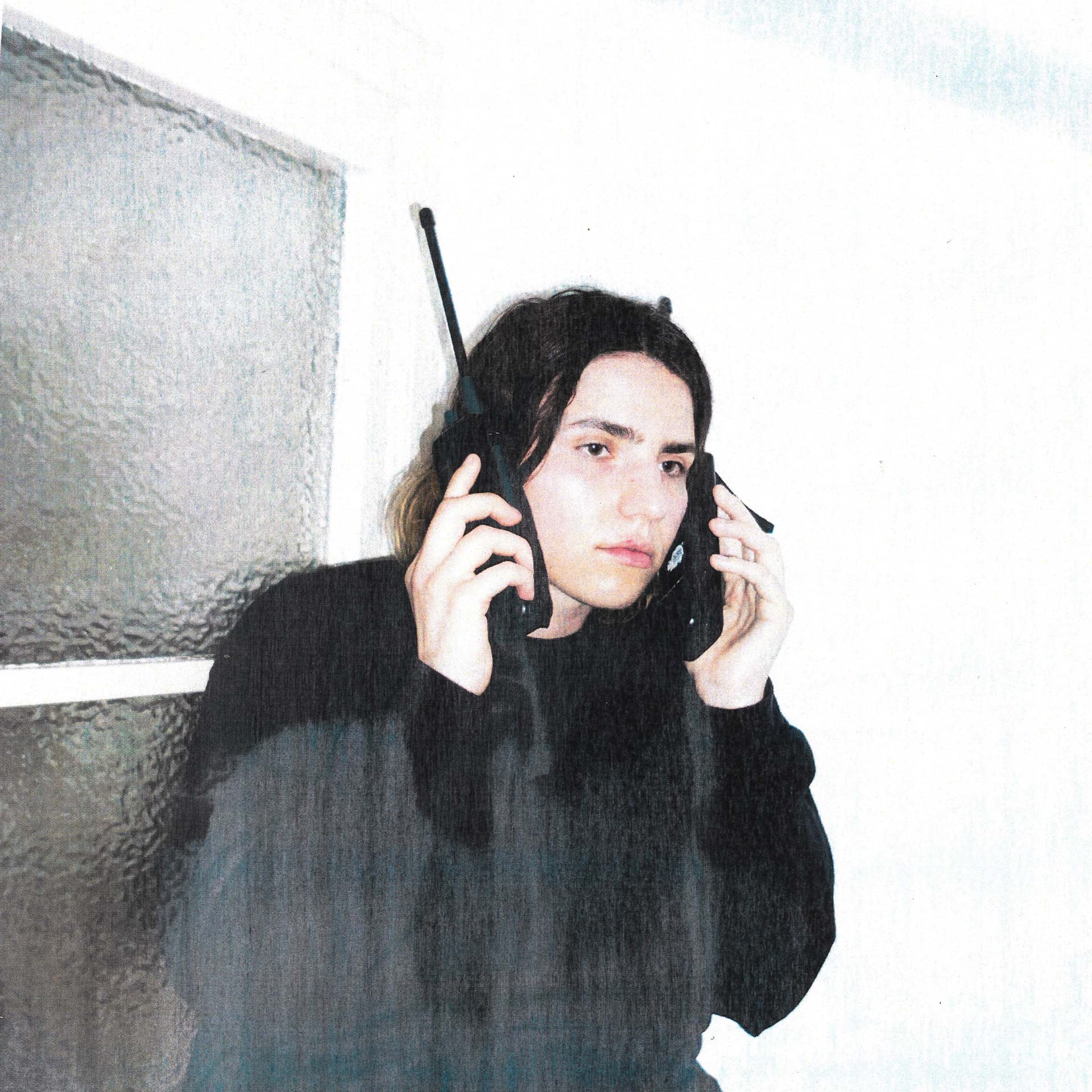 Person hält zwei Telefone am Ohr und steht vor einem Fenster.