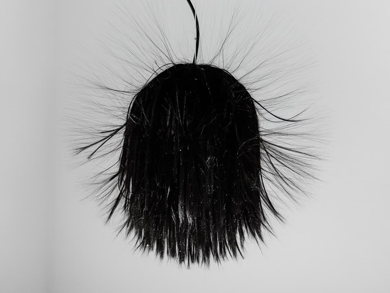 Ein stacheliges, schwarzes, kugelförmiges Objekt mit langen, dünnen Auswüchsen hängt an einem Kabel vor einem schlichten weißen Hintergrund.
